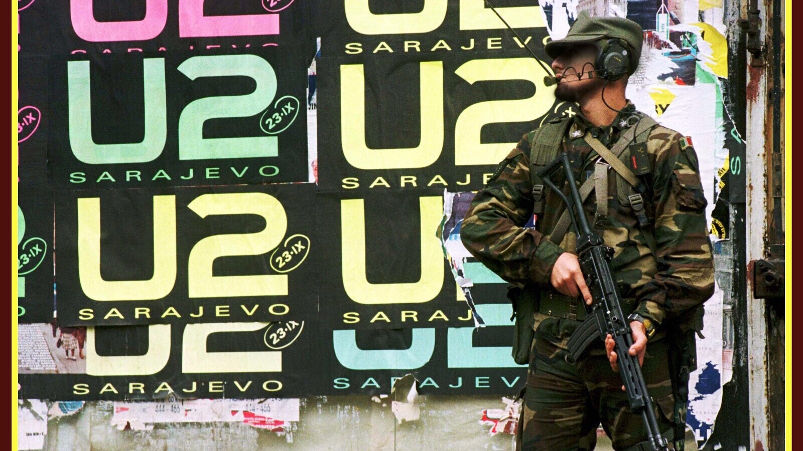 An Italian peacekeeper holds his rifle as he stands in front of wall covered with U2 posters in Sarajevo, September 21, 1997 ahead of the band’s performance at the Kosevo Stadium